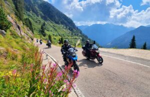 Eine Gruppe Motorradfahrer ist in den Alpen auf einer kurvenreichen Straße unterwegs.